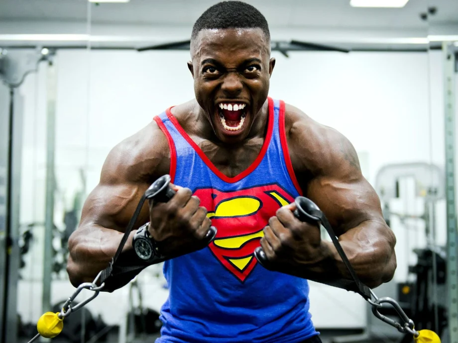 Man in Superman tank top doing cable crossovers in gym Peoples CBD - Make Life Better Everyday!